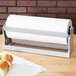 A Bulman gray steel paper dispenser on a table with a sandwich and a roll of paper towels.