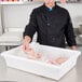 A person's hand holding a plastic bag of chicken in a white Cambro container.