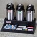 A black tray with a Cambro Triple Airpot and Condiment Station holding three coffee pots and condiments.