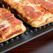 Two pieces of pizza on a charcoal rectangular pizza tray.