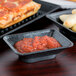 A black rectangular dish with red sauce on a table with a pizza.
