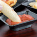 A person dipping food into a rectangular condiment server filled with sauce.