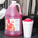 A jug of Carnival King Fruit Punch Slush Syrup next to a cup of slushy.