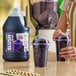 A gallon jug of Carnival King grape slush syrup concentrate next to two cups of prepared grape slushies.