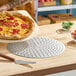 A round, perforated metal pizza disk on a wooden countertop.