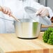 A person using a Vollrath aluminum sauce pan to cook on a stovetop.