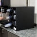 A woman filling a glass with a Vollrath countertop cup dispenser.