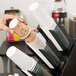 A hand using a Vollrath black countertop cup and lid organizer to dispense paper cups.