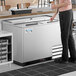 A man standing next to an Avantco stainless steel glass froster in a professional kitchen.