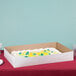 A white full sheet cake in a white bakery box on a table.