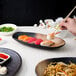 A person using chopsticks with a 10 Strawberry Street Whittier Nagoya oval platter of sushi.