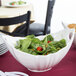 A white boat bowl filled with salad on a table.