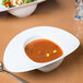 A white oval porcelain bowl filled with soup on a table.