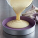 A person pouring white cake batter into a Chicago Metallic round cake pan.