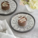 Two plates with chocolate desserts on silver foil lace doilies.