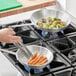 A person cooking carrots and brussels sprouts in a Choice aluminum fry pan on a stove.