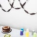 A table set with a chocolate cake and purple and blue cups with black velvet streamers on the table.