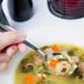 A person holding a Libbey stainless steel bouillon spoon over a bowl of soup.