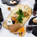 An American Metalcraft faux rustic wood melamine serving board with food and wine on a table.