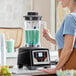A commercial blender with a digital touchpad control panel and a large clear container filled with a green beverage.