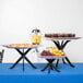 A Tablecraft black fold-a-way riser set with trays of food on a table.