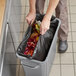 A person putting a Lavex Li'l Herc black garbage bag into a trash can full of garbage.