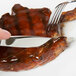 A person using a Libbey stainless steel steak knife and fork to cut a piece of meat on a white plate.