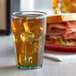 A jade plastic tumbler filled with ice tea on a table with a sandwich.