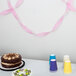 A table with a chocolate cake and pink streamers on it.