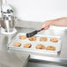 A hand holding a spatula over Vollrath Wear-Ever bun pan of cookies.