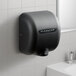 A graphite XLERATOR hand dryer on a white tile wall above a white sink.