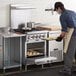 A man in a professional kitchen using a Cooking Performance Group 24" range to put food in the oven.