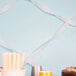 A table with a white cake and silver cups with white streamers on the wall.