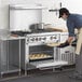 A man in a professional kitchen using a Cooking Performance Group 6 burner range with an oven to cook food.