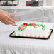 A hand using a D&W Fine Pack plastic container to cover a frosted sheet cake.