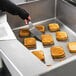 A person cutting up toasted sandwiches in a Vulcan tilt skillet on a counter.