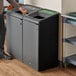 A man standing next to a Rubbermaid Stenni grey recycling container.