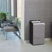 A Rubbermaid Stenni grey square waste container in a hallway.