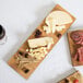 An American Metalcraft carbonized bamboo serving board with cheese and olives on a wooden surface.