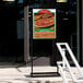 A black double sided freestanding sign holder with a poster of a pizza on it.