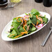 A plate of salad with spinach, carrots, and onions on a 10 Strawberry Street white oval porcelain plate.