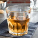 An Arcoroc stackable rocks glass filled with brown liquid on a table.