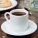 A white 10 Strawberry Street porcelain espresso cup full of brown coffee on a saucer.