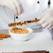 A person in white gloves dipping a Snyder's of Hanover pretzel rod into a bowl of chocolate.