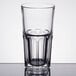 An Arcoroc stackable beverage glass filled with a clear liquid on a table.