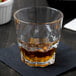 An Arcoroc stackable rocks glass filled with brown liquid on a table.