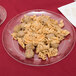 A WNA Comet clear plastic plate with a white design holding pasta and meatballs on a red tablecloth.