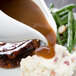 A plate of food with gravy being poured over mashed potatoes and green beans using a white gravy boat.