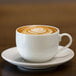 A white 10 Strawberry Street porcelain coffee cup on a saucer with a heart shaped latte.