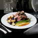 A close-up of a 10 Strawberry Street Classic White porcelain dinner plate with meat and vegetables and silverware.